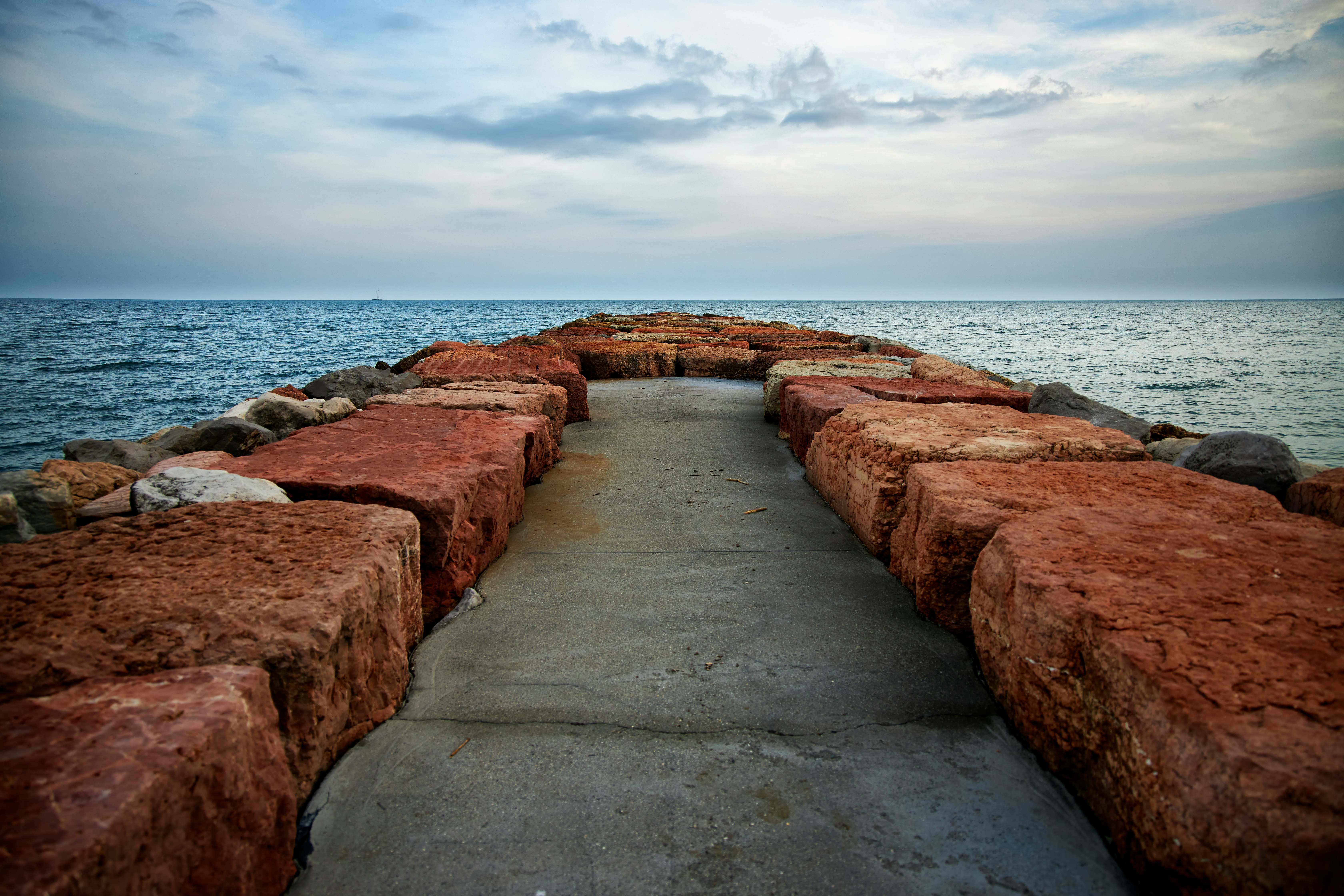 brown concrete pathway on sea shore under cloudy sky during daytime